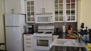 Cocina compacta con muebles blancos, un refrigerador, microondas, estufa y pileta.