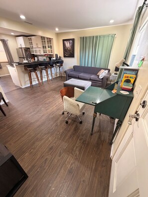 Una sala de estar moderna con un sofá, una mesa de centro y un escritorio con una lámpara. Hay una zona de cocina con un refrigerador y una mesa de comedor con sillas.