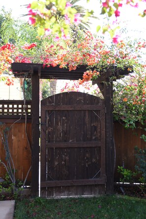 Une porte en bois surmontée d’une arche également en bois, le tout entouré d’une végétation luxuriante et de plantes en fleurs.