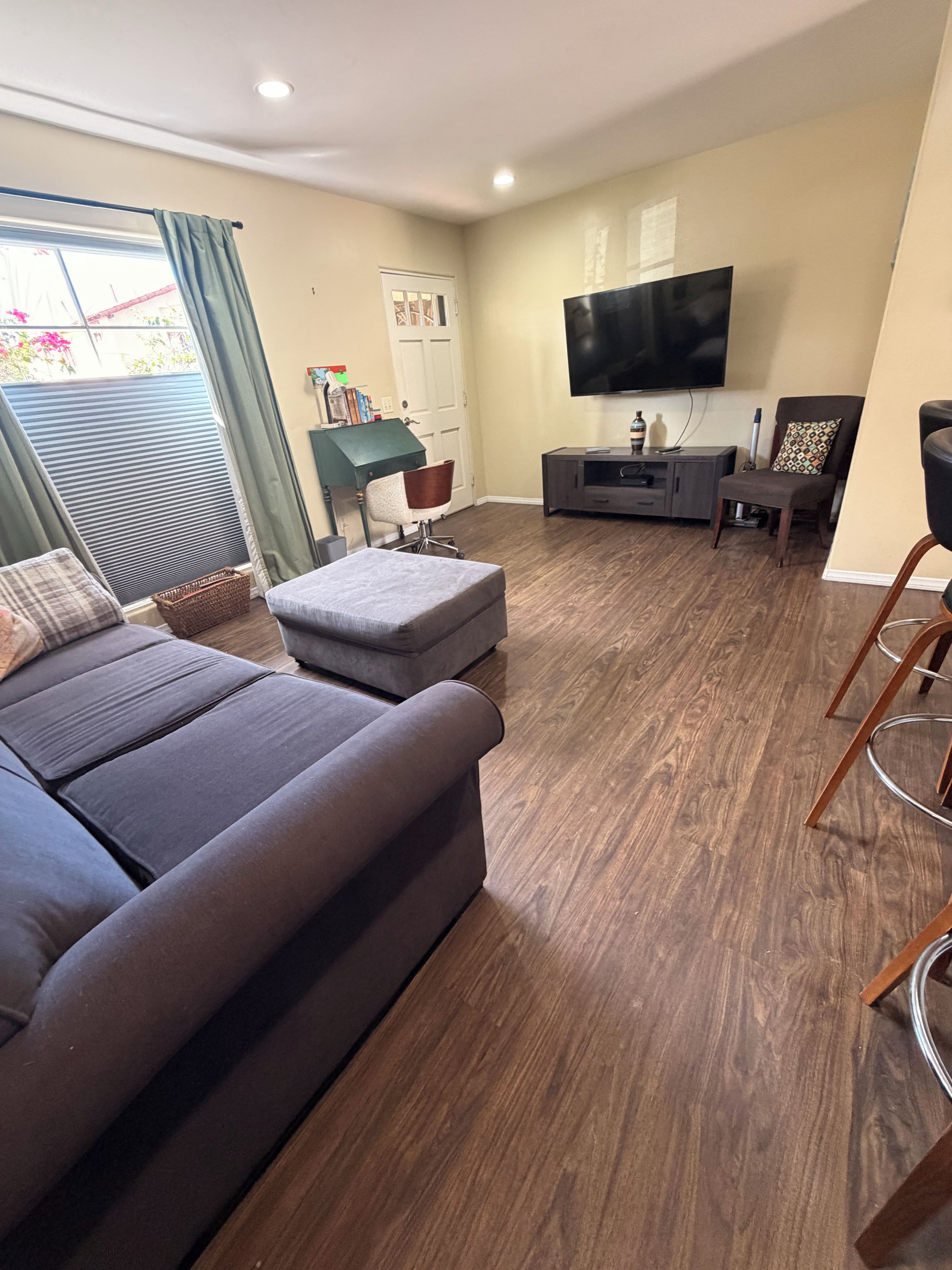 Un salon moderne avec un canapé d’angle gris, un téléviseur à écran plat fixé au mur et un plancher en bois.