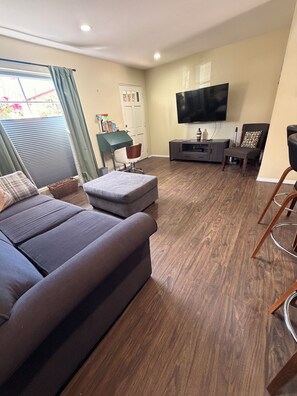 Un salon moderne avec un canapé d’angle gris, un téléviseur à écran plat fixé au mur et un plancher en bois.