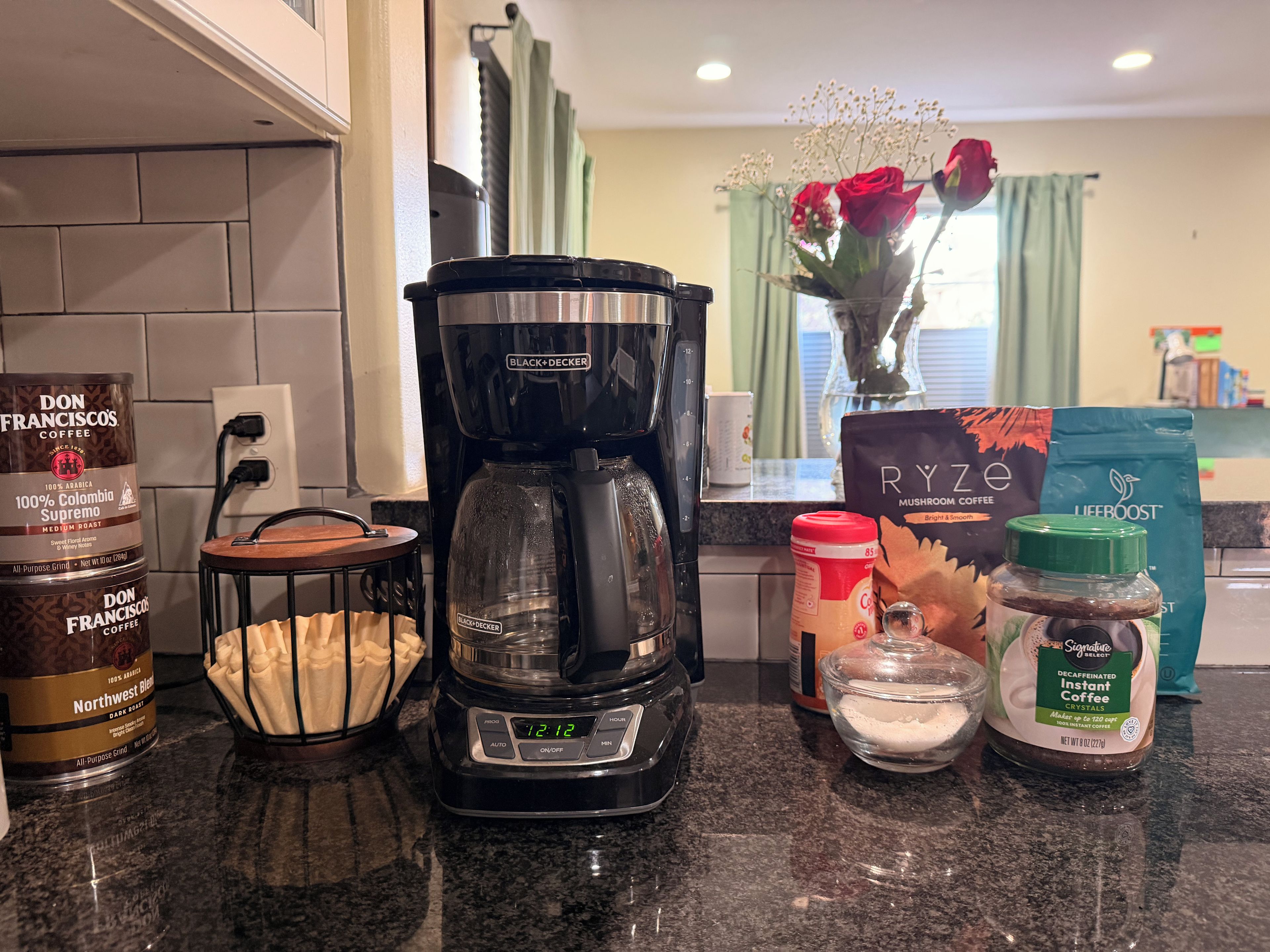 Un plan de travail de cuisine avec une machine à café, des grains de café, un moulin à café et un paquet de dosettes de café.