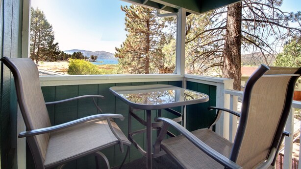 A balcony with two chairs and a table, overlooking a scenic landscape with trees and a body of water.