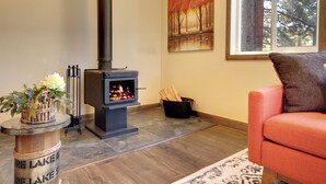 A cozy living room with a wood-burning stove, a comfortable orange sofa, and a painting of trees on the wall.