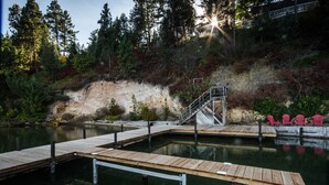 A wooden dock extending into a calm body of water, surrounded by dense forest and a rocky hillside. - Lakefront Home With Hot Tub, Dock, Great Views From The Living Room & Bedrooms  (Somers)