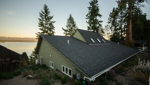 A house with a sloped roof, a fenced yard, and a view of a lake and mountains in the background. - Lakefront Home With Hot Tub, Dock, Great Views From The Living Room & Bedrooms  (Somers)