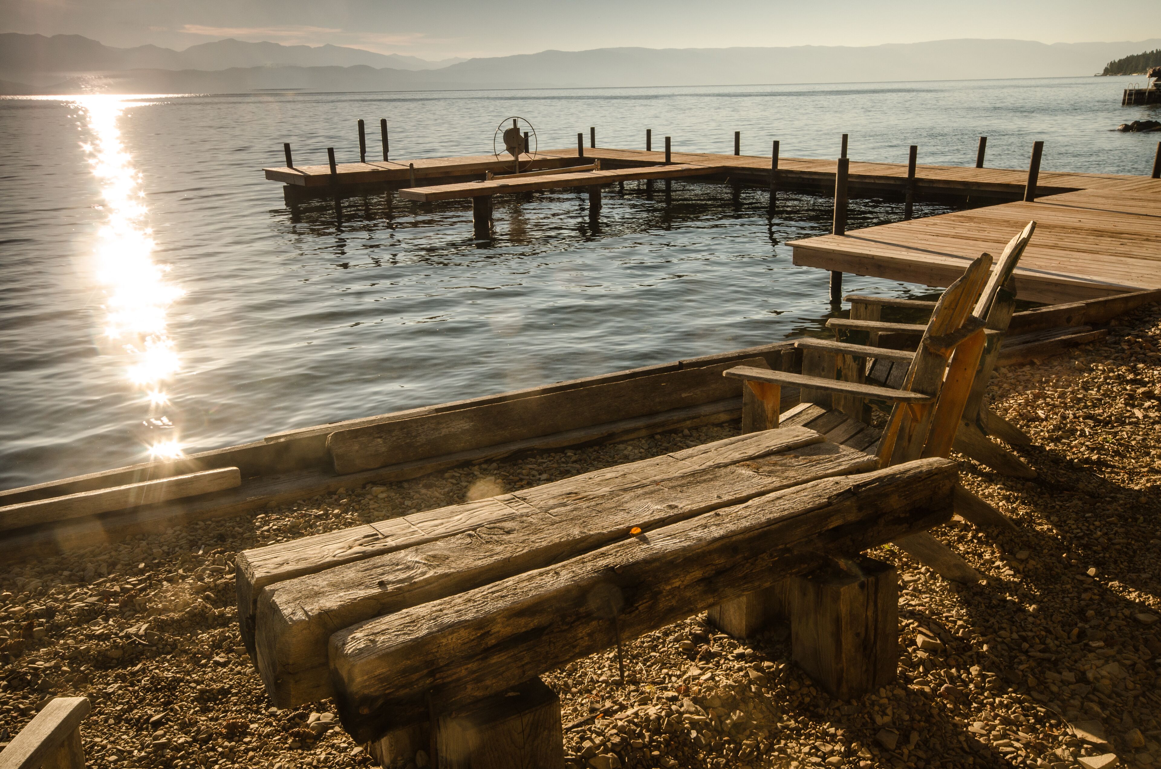 Une jetée en bois s’étendant sur une étendue d’eau calme, avec un banc et une table à proximité.