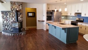 A modern kitchen with a stone fireplace, a large island, and white cabinetry. - Lakefront Home With Hot Tub, Dock, Great Views From The Living Room & Bedrooms  (Somers)
