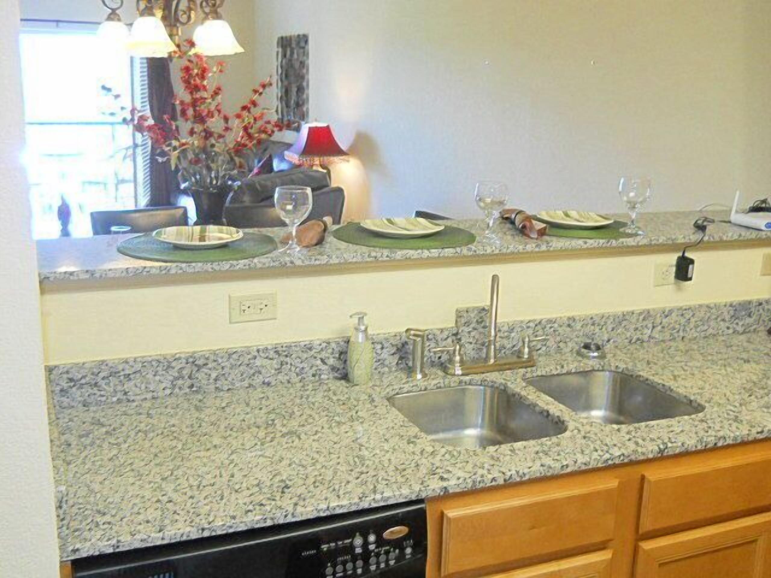 A kitchen with granite countertops, stainless steel sinks, and wooden cabinets.