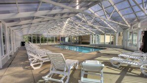 Ein überdachter Poolbereich mit weißen Liegestühlen, ein klares Schwimmbecken und eine Glaskonstruktion als Decke.