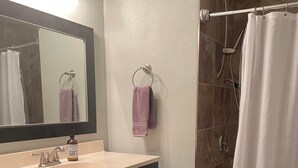 A bathroom with a vanity, a mirror, a shower with a curtain, and a dark rug. - Downtown/Corporate/Individuals (Anchorage)