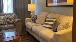 A modern living room with a beige sofa, a glass coffee table, and a lamp. - Downtown/Corporate/Individuals (Anchorage)