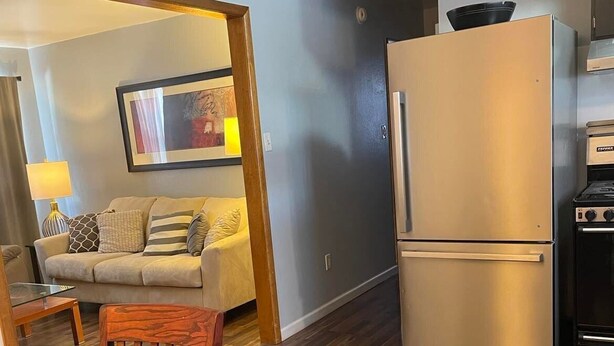 A compact kitchen with a stainless steel refrigerator, a built-in oven, and a wooden dining table with chairs. - Downtown/Corporate/Individuals (Anchorage)