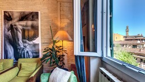 A room with a large window, a green sofa, a lamp, and a painting on the wall. - CHARMING HIDEAWAY IN FLORENCE OLD TOWN (Firenze)