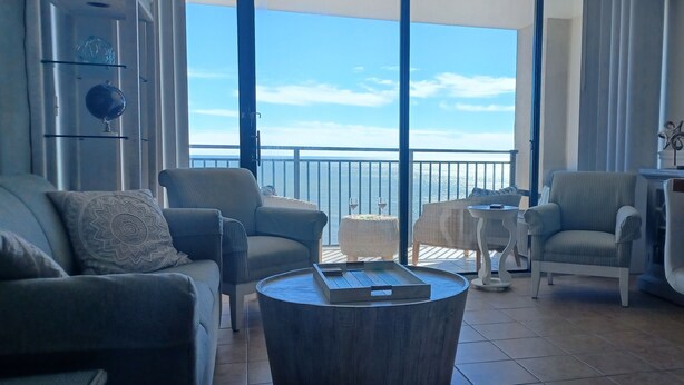 A spacious balcony with a view of the sea, furnished with a sofa, chairs, and a small table.
