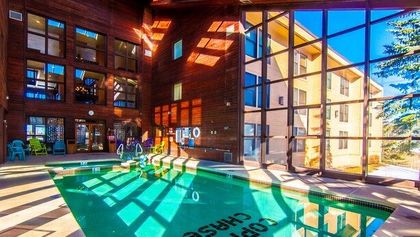Una piscina con interior iluminado por el sol, rodeada de grandes ventanales y fachada de madera.