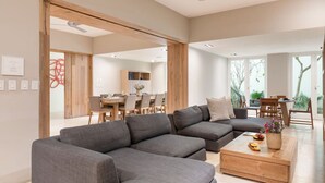 Una sala moderna con un sofá seccional gris, una mesa de centro de madera y un comedor con sillas y mesa de madera.