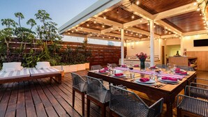 Un área de comedor al aire libre con cubierta de madera, sillas de mimbre y una mesa lista para una comida.