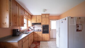 Una cocina con armarios de madera, cafetera, lavamanos y refrigerador.