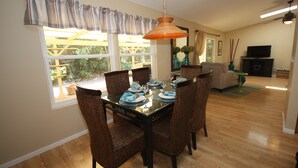 A dining area with a glass table, wicker chairs, and a hanging pendant light. - Magic Sands Home, Steps From The Beach! Air Conditioned! 3D tour to view space (Kailua-Kona)