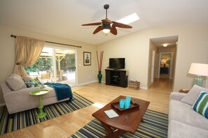 A living room with a sofa, coffee table, TV, and a ceiling fan. - Magic Sands Home, Steps From The Beach! Air Conditioned! 3D tour to view space (Kailua-Kona)