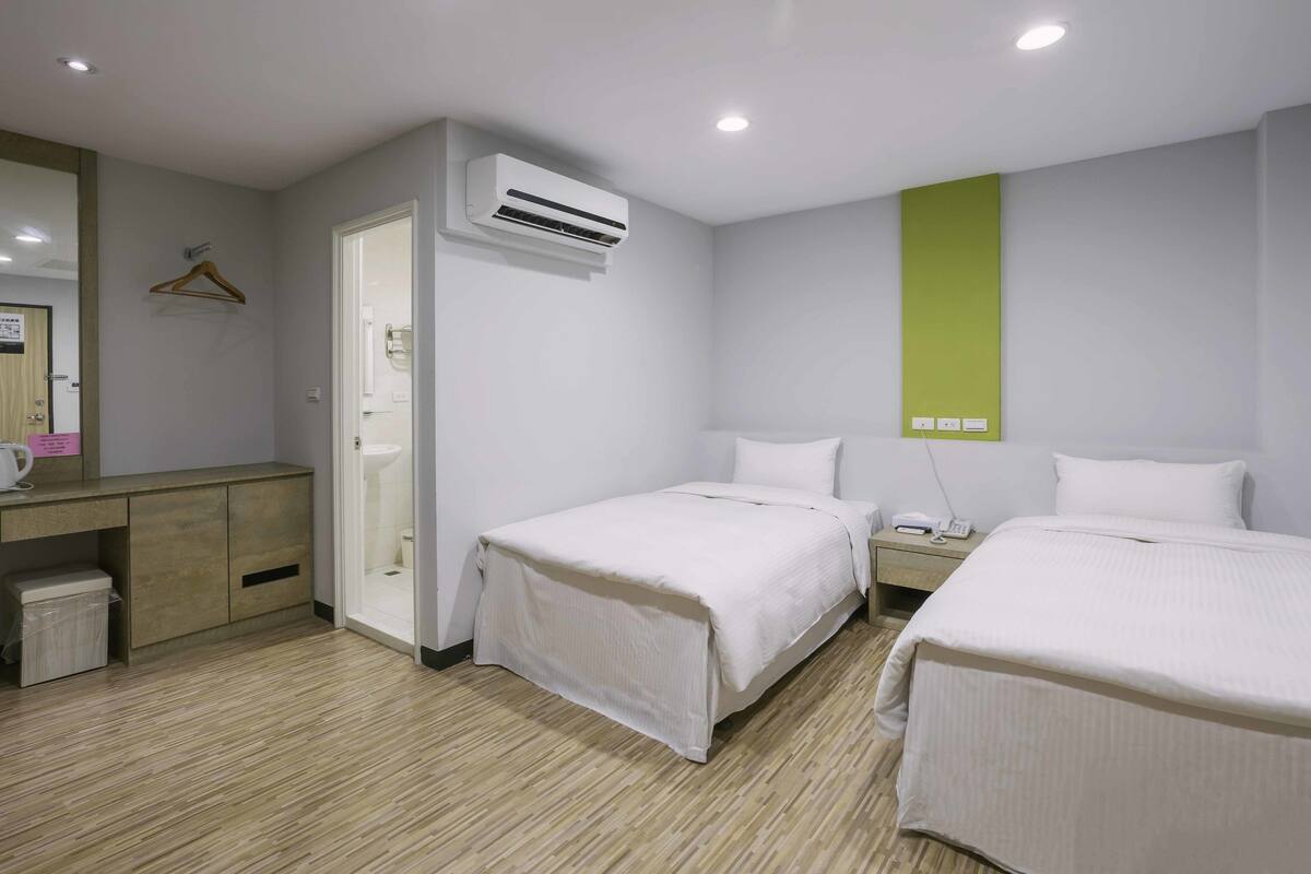 Una habitació d'hotel amb dos llits, una taula de nit amb un telèfon, un petit cistell de brossa i un aire condicionat fixat a la paret.