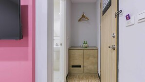 Un pasillo estrecho con una pared rosa, un armario de madera con botellas y un perchero de madera.