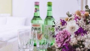 Dos botellas verdes y dos vasos de cristal sobre una mesa con un arreglo floral.