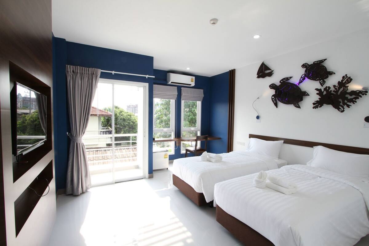 Habitación de hotel con dos camas, televisor, balcón con vistas y decoración en la pared.