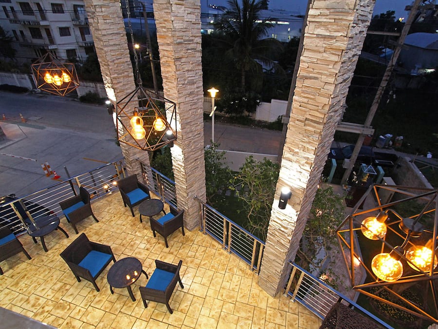 An outdoor seating area with wicker furniture and a tiled floor, surrounded by stone pillars and illuminated by hanging light fixtures.