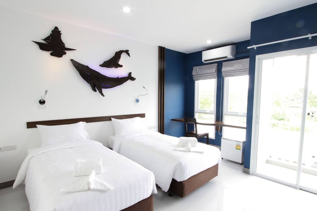Habitación de hotel con dos camas, un ventanal grande y un equipo de aire acondicionado instalado en la pared.