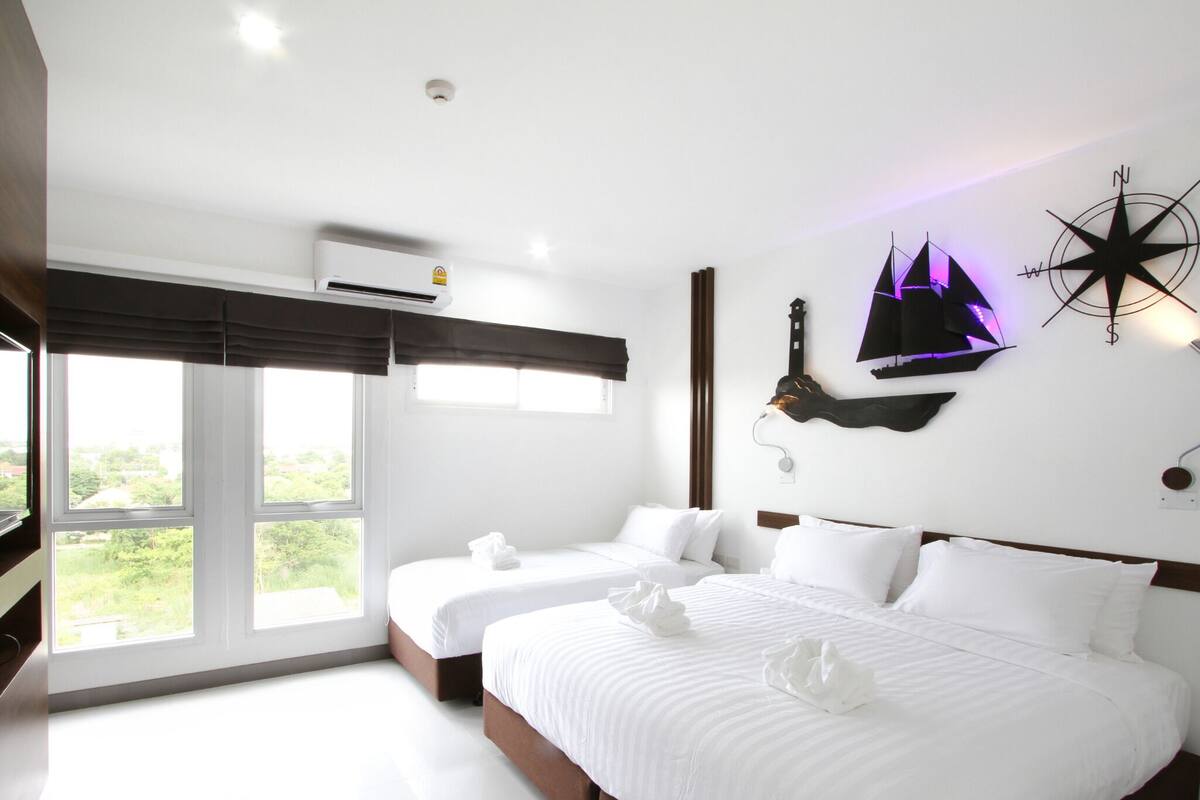 Habitación de hotel con dos camas, un ventanal grande, aire acondicionado de pared y un adorno mural.