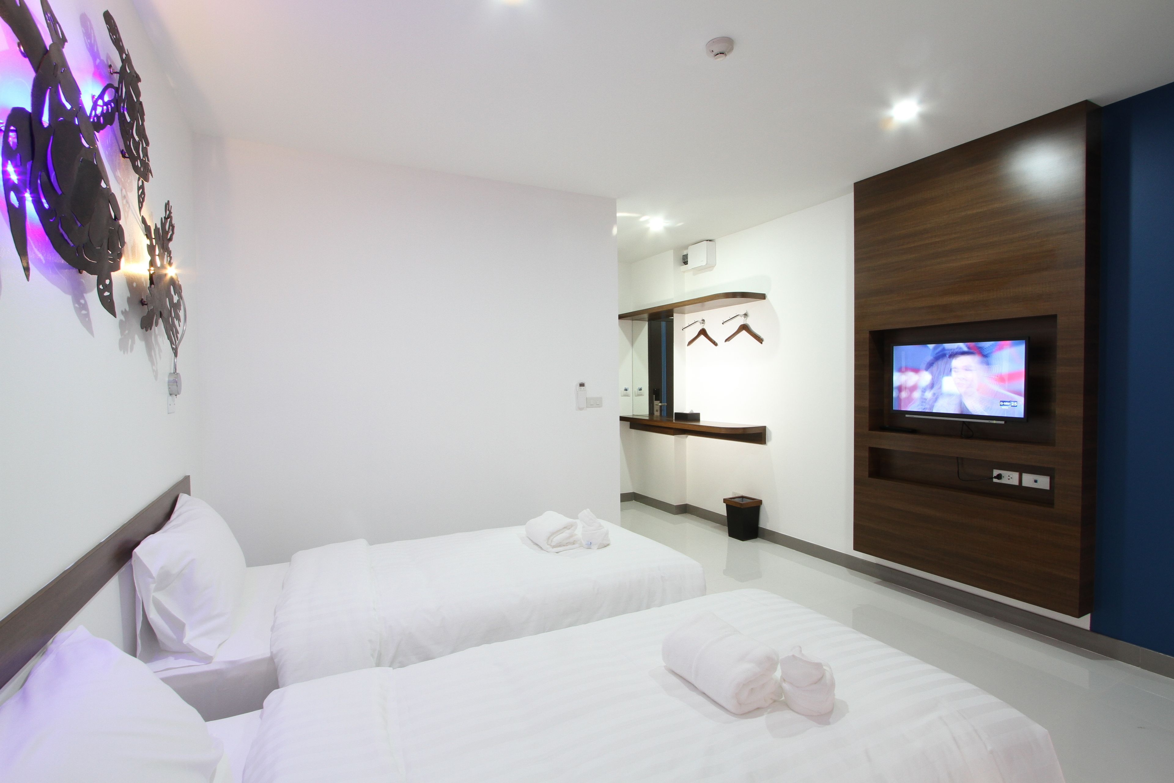A hotel room with two beds, a TV, a wall-mounted shelf with hangers, and a decorative light fixture.