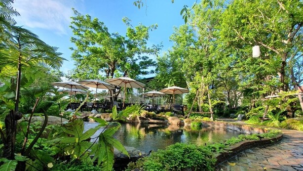 Un giardino con uno stagno, area salotto esterna e vegetazione rigogliosa.