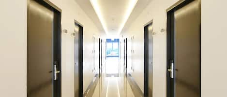 A modern hotel corridor with a reflective floor, evenly spaced doors, and recessed lighting.