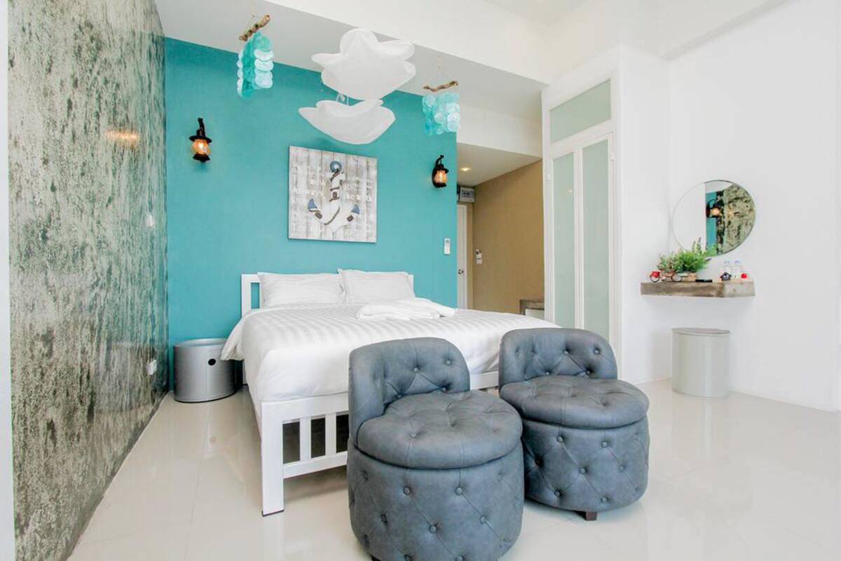 A modern bedroom with a white bed, teal accent walls, and a large mirror.
