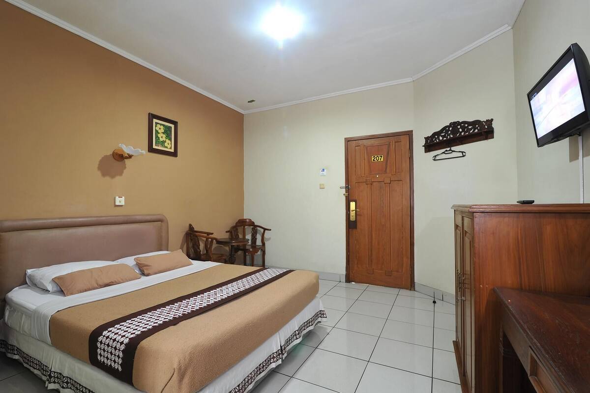 Een hotelkamer met een bed, een houten deur, een televisie en een kleine tafel.