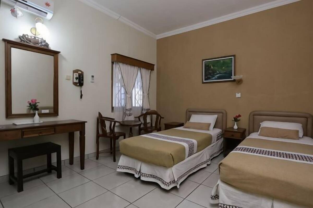 Een hotelkamer met twee bedden, een bureau, een stoel, een spiegel en een schilderij aan de muur.