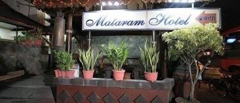 A hotel entrance with a sign reading "Malam Hotel" and several potted plants in front.