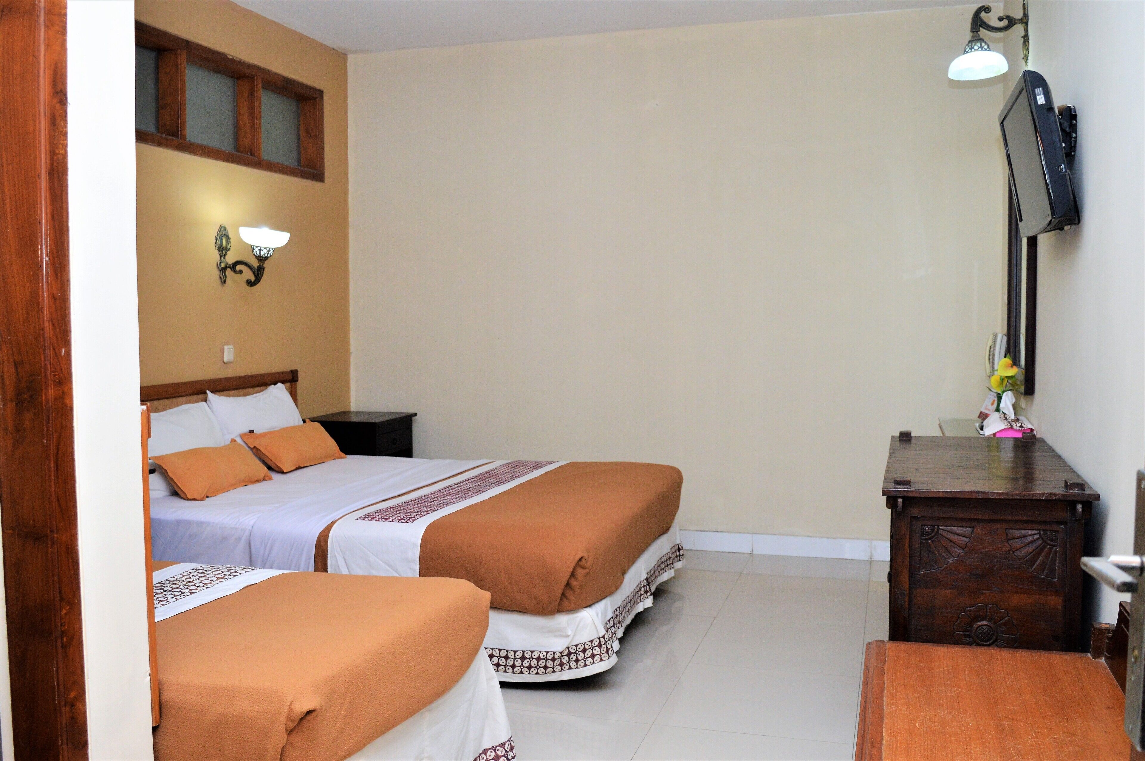 Une chambre d’hôtel avec deux lits, une table de chevet en bois, un bureau et une lampe fixée au mur.