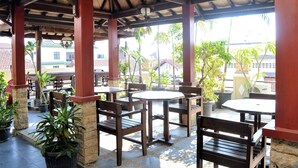An outdoor patio area with wooden tables and chairs, surrounded by potted plants. - Hotel Mataram 2 Malioboro (Yogyakarta)