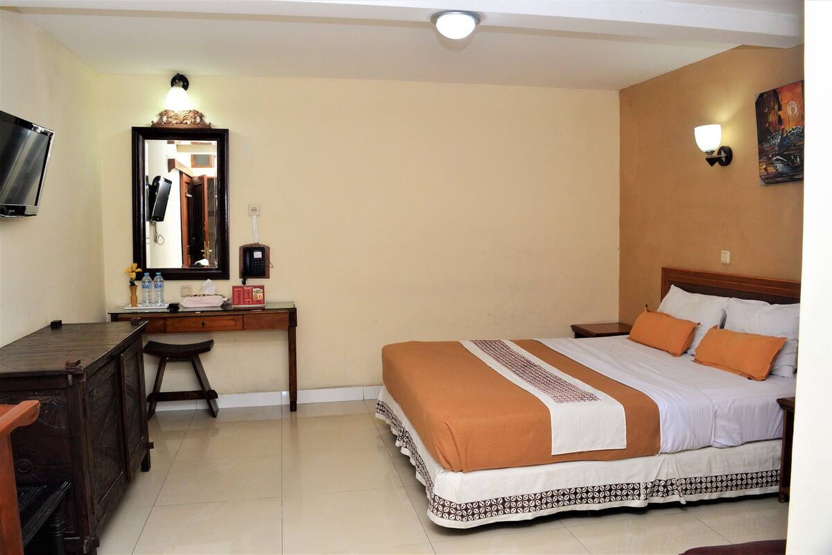 Une chambre d’hôtel comprenant un lit, un bureau, une chaise, un miroir, une télévision et un luminaire fixé au mur.