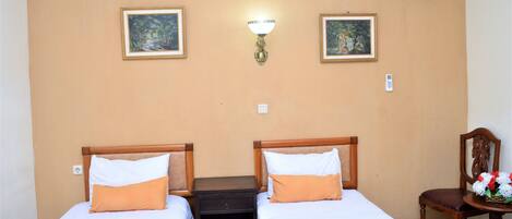 Habitación de hotel con dos camas, una mesita de noche, una lámpara de pared y una silla con un arreglo floral.