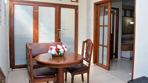 A room with a wooden table and chairs, a flower arrangement, and a bed with a patterned bedspread. - Hotel Mataram 2 Malioboro (Yogyakarta)