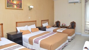 A hotel room with three beds, a painting on the wall, a nightstand, an air conditioning unit, and a window with curtains. - Hotel Mataram 2 Malioboro (Yogyakarta)