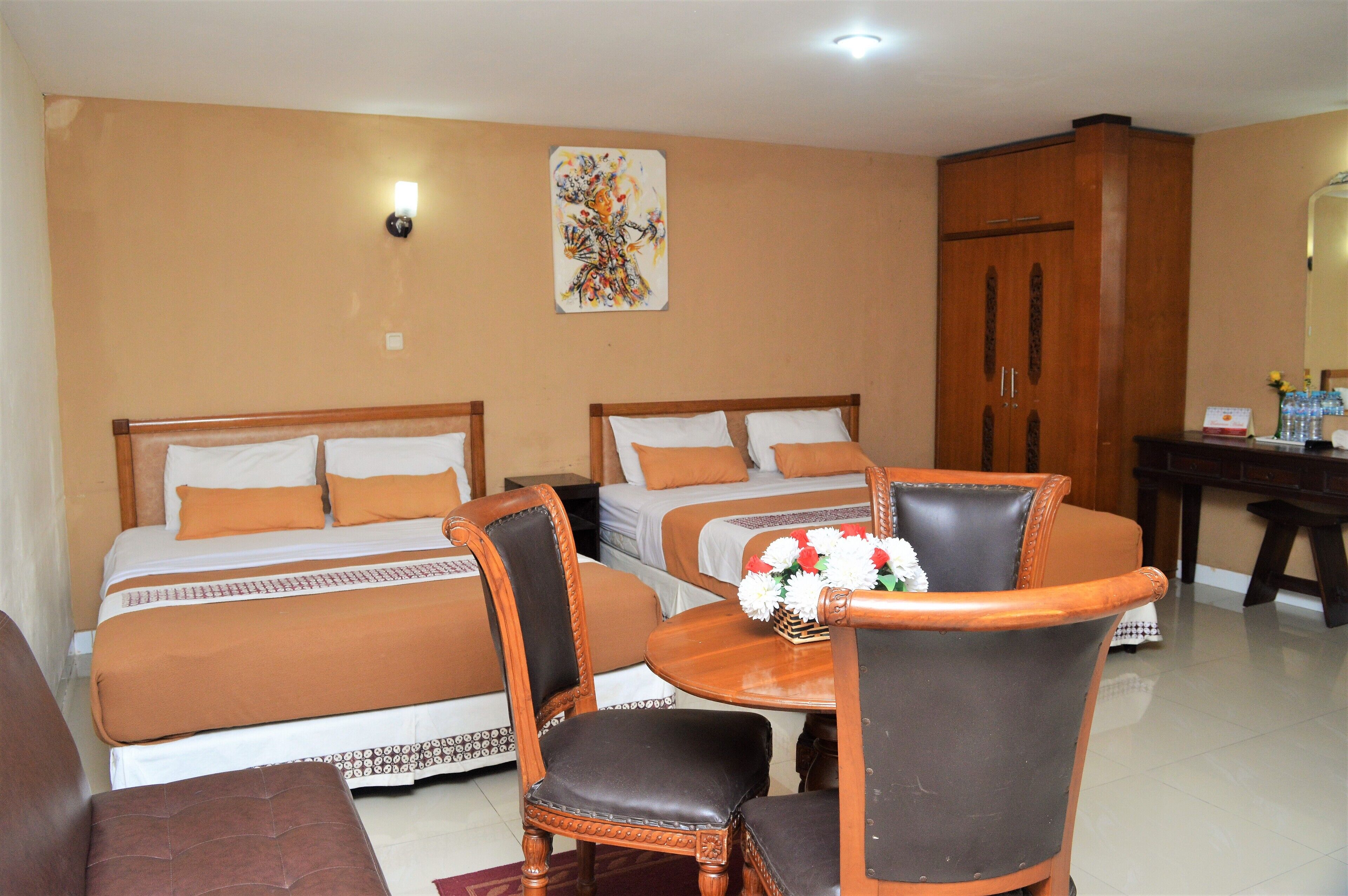 A hotel room with two beds, a wooden table with chairs, a desk, and a cabinet.