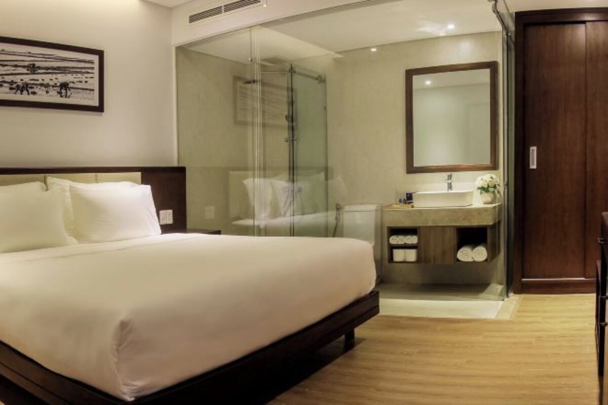 A hotel room with a bed, a glass-enclosed shower, a sink, and a mirror.