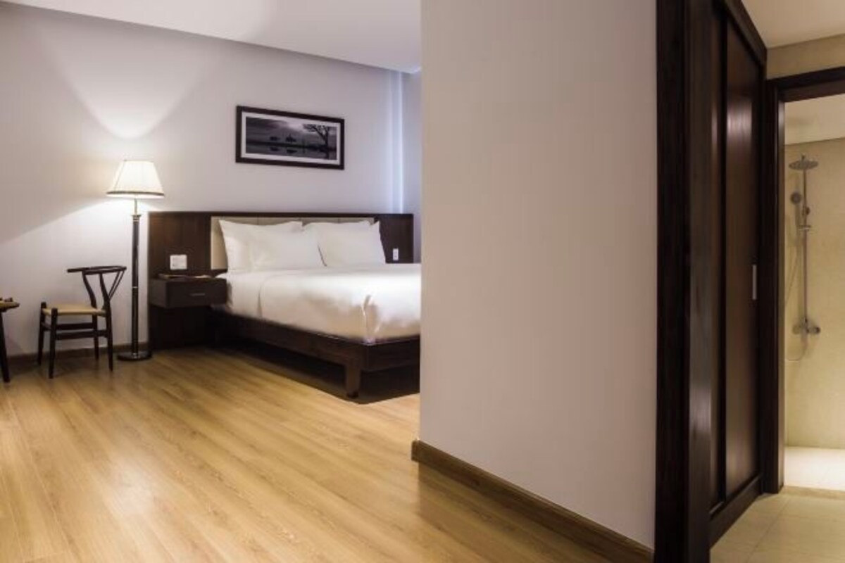 A hotel room with a bed, a chair, a desk, a lamp, and a framed picture on the wall.