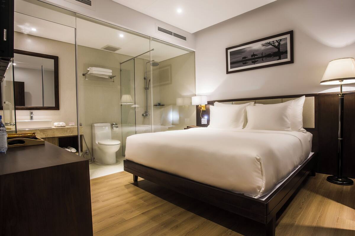 Quarto de hotel com cama, mesa de cabeceira, abajur e um quadro na parede.