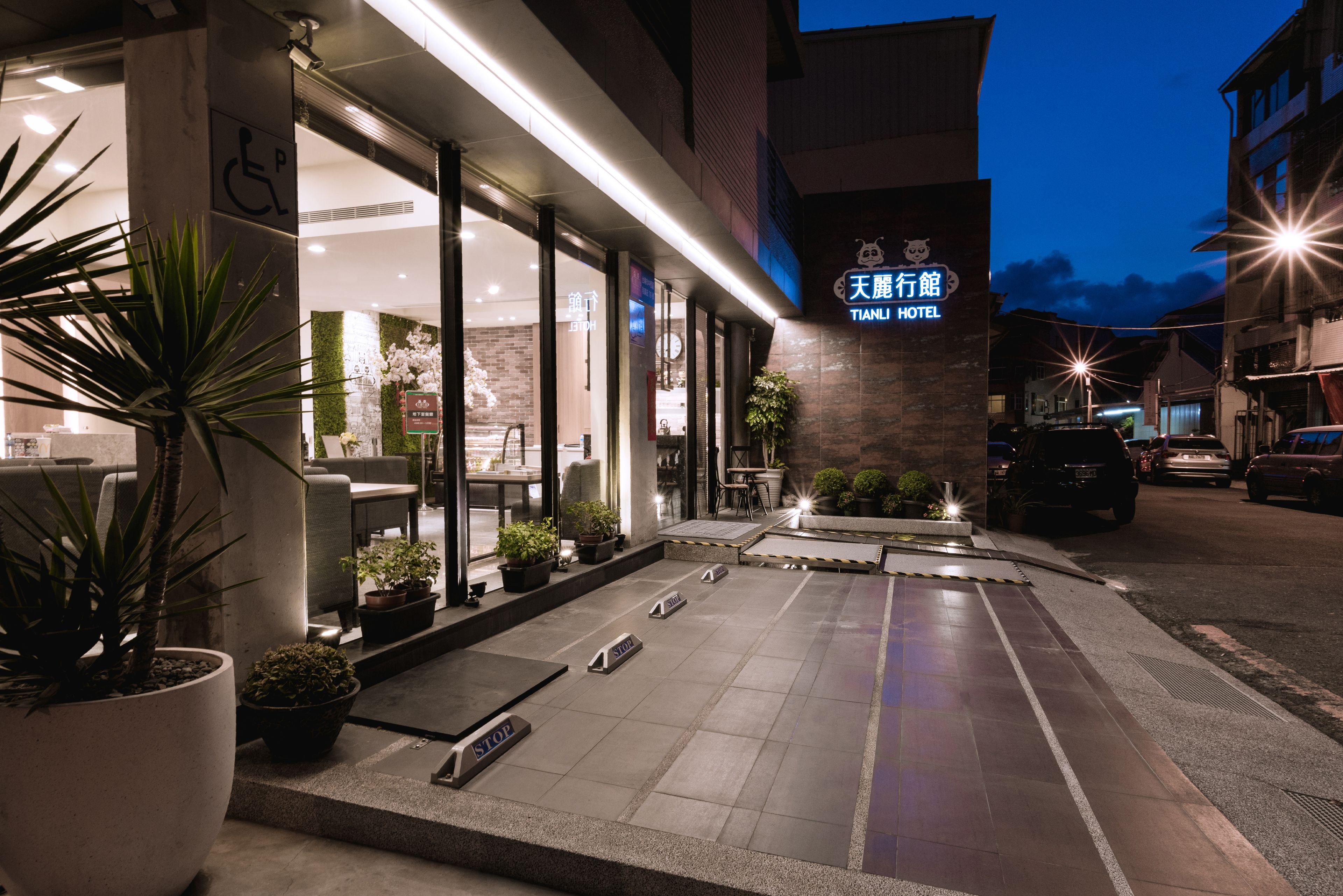 A hotel entrance with a sign reading "Tianli Hotel" and a wheelchair accessibility symbol. There are potted plants and a ramp leading to the entrance.